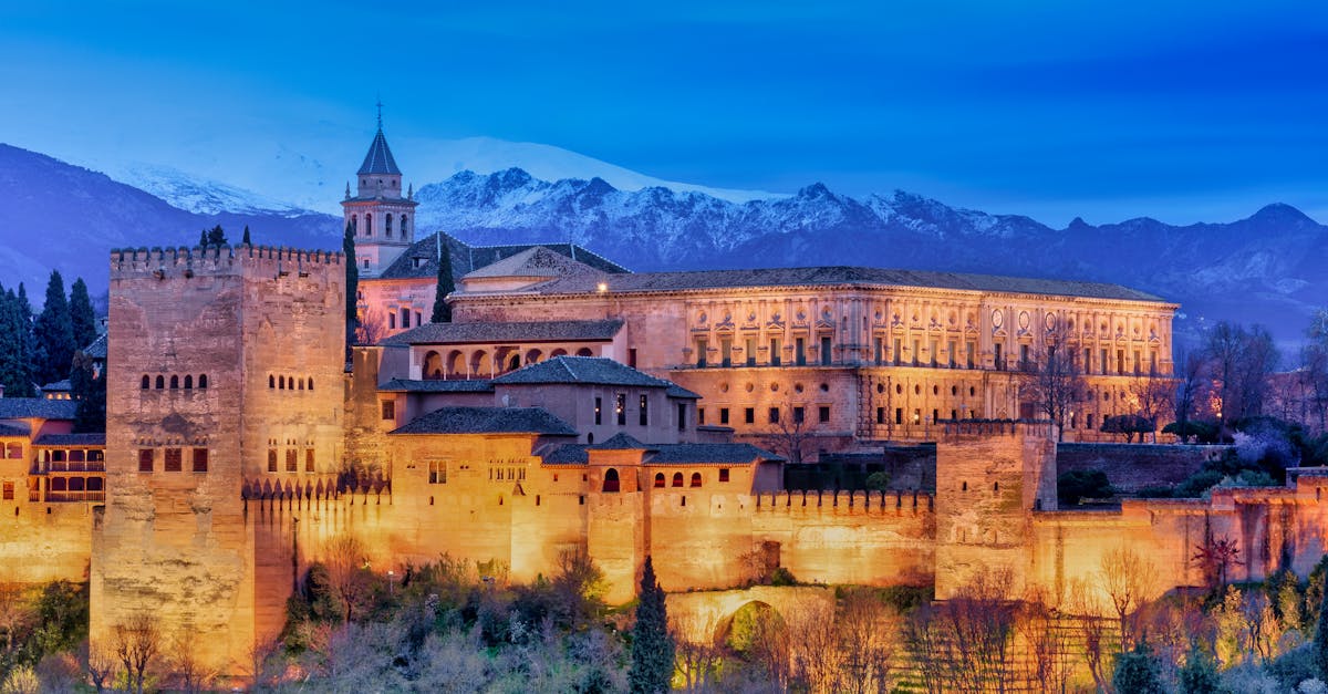 Stunning view of the illuminated Alhambra Palace with snowy mountains in Granada.